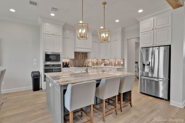 kitchen featuring white cabinetry, stainless steel appliances, light stone countertops, and a kitchen island with sink