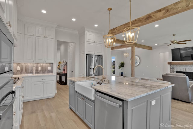 kitchen with hanging light fixtures, a center island with sink, light wood-type flooring, white cabinetry, and appliances with stainless steel finishes