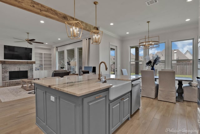 kitchen with a center island with sink, sink, light stone countertops, gray cabinets, and a fireplace