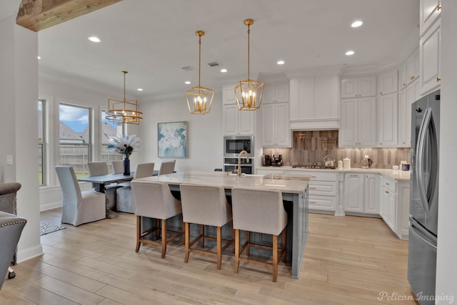 kitchen featuring white cabinetry, hanging light fixtures, stainless steel appliances, and a center island with sink