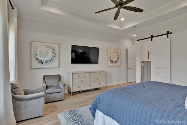 bedroom featuring ceiling fan, a barn door, a tray ceiling, light hardwood / wood-style flooring, and ornamental molding