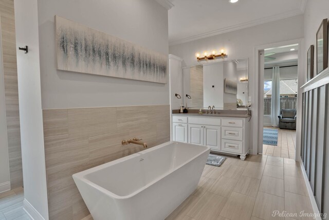 bathroom with tile walls, vanity, ornamental molding, and a bath