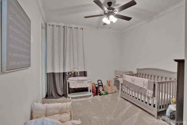 carpeted bedroom with ceiling fan, ornamental molding, and a nursery area