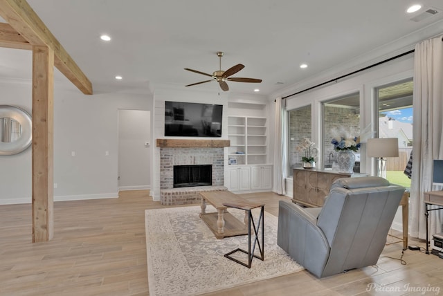 living room with ceiling fan, a brick fireplace, light hardwood / wood-style flooring, built in shelves, and crown molding