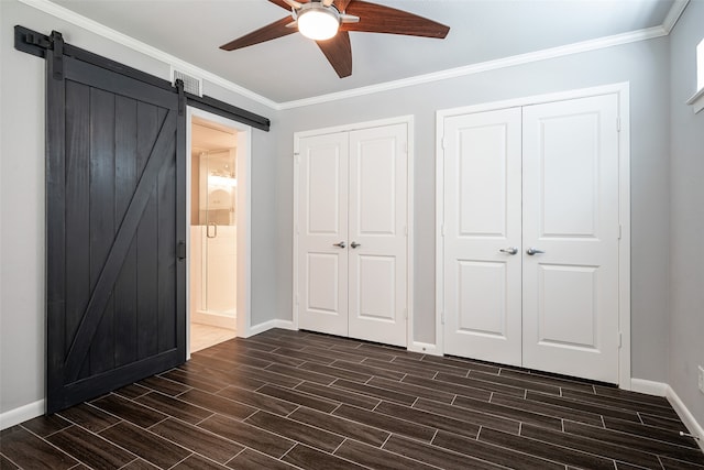 unfurnished bedroom featuring ceiling fan, multiple closets, ornamental molding, and a barn door