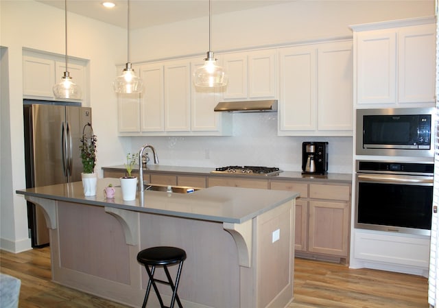 kitchen with white cabinetry, appliances with stainless steel finishes, hanging light fixtures, and a center island with sink