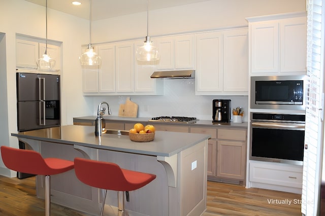 kitchen featuring stainless steel appliances, white cabinetry, and a center island with sink