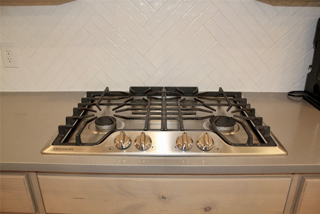 room details featuring stainless steel gas stovetop, light brown cabinets, and decorative backsplash