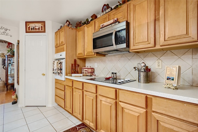 kitchen with black electric stovetop, tasteful backsplash, stainless steel microwave, light tile patterned flooring, and oven