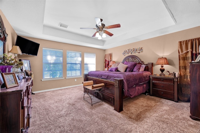 carpeted bedroom with a tray ceiling, a ceiling fan, visible vents, and baseboards