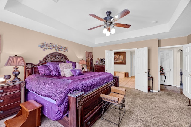 bedroom with carpet floors, ceiling fan, a tray ceiling, and arched walkways