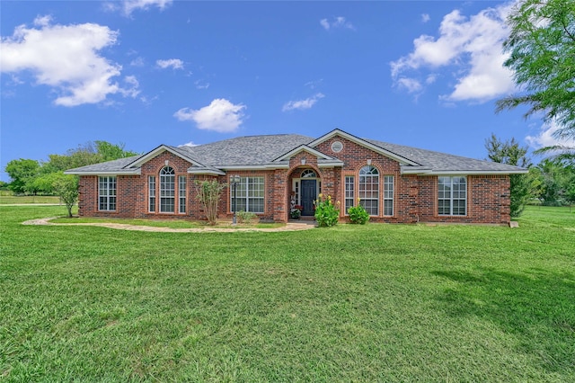 ranch-style home with brick siding, roof with shingles, and a front yard