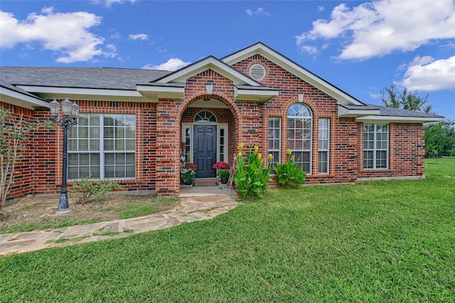 ranch-style house with a shingled roof, a front lawn, and brick siding