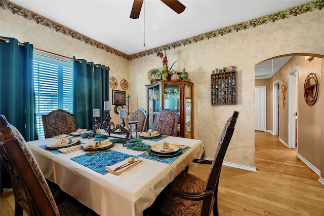 dining room featuring a ceiling fan, light wood-style flooring, arched walkways, and baseboards