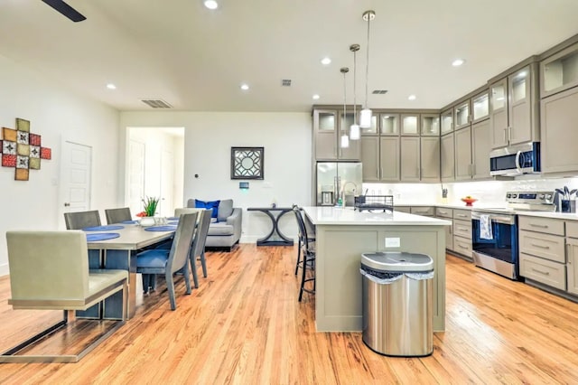 kitchen with stainless steel appliances, decorative light fixtures, light hardwood / wood-style floors, a breakfast bar area, and an island with sink