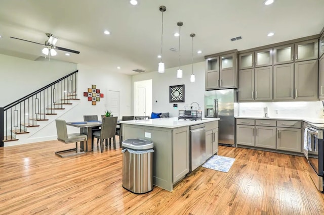 kitchen featuring stainless steel appliances, a kitchen island with sink, ceiling fan, decorative light fixtures, and light hardwood / wood-style flooring