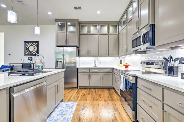 kitchen featuring sink, tasteful backsplash, light hardwood / wood-style floors, decorative light fixtures, and appliances with stainless steel finishes