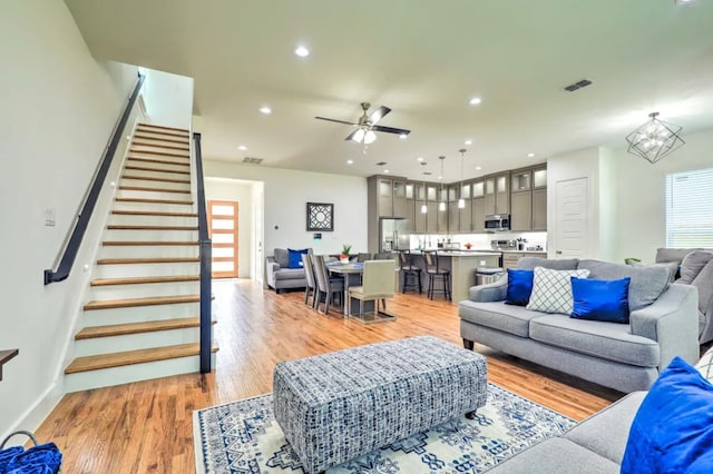 living room featuring ceiling fan with notable chandelier and light hardwood / wood-style flooring