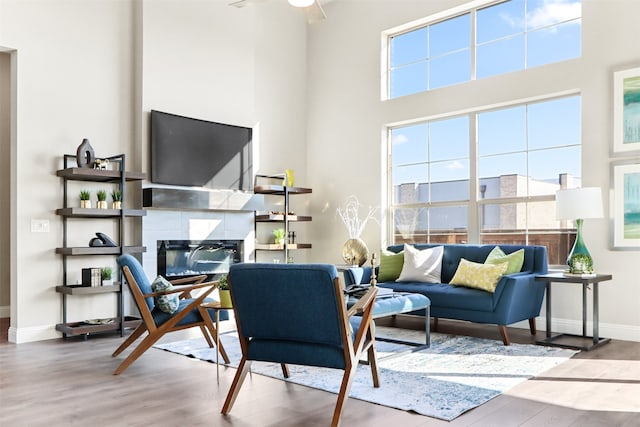 interior space featuring a high ceiling, ceiling fan, a tile fireplace, and hardwood / wood-style floors