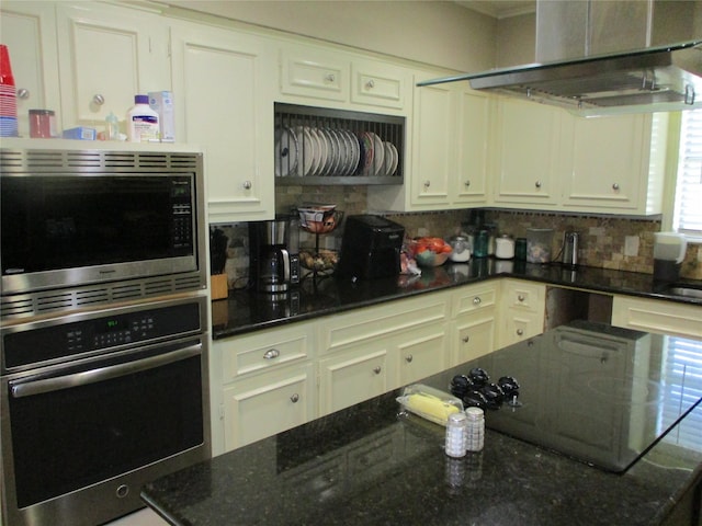 kitchen featuring exhaust hood, stainless steel appliances, dark stone countertops, and backsplash