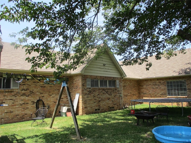 back of property featuring a lawn and a trampoline