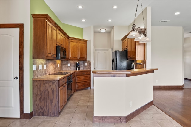 kitchen featuring light hardwood / wood-style flooring, black appliances, tasteful backsplash, kitchen peninsula, and hanging light fixtures