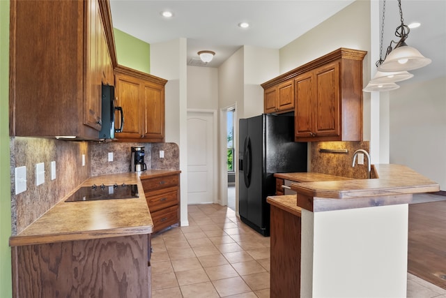 kitchen with black appliances, hanging light fixtures, light hardwood / wood-style floors, kitchen peninsula, and backsplash