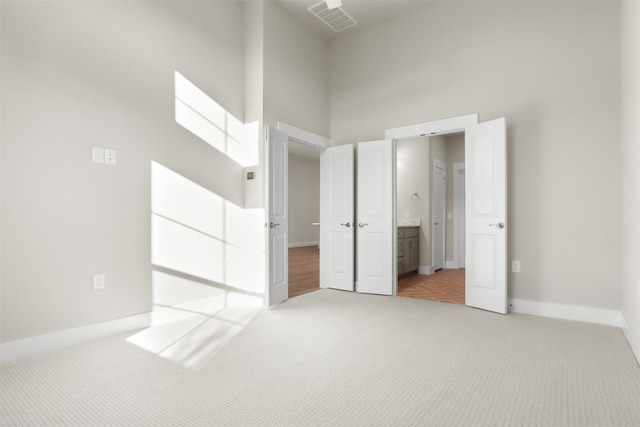 unfurnished bedroom with carpet, ensuite bathroom, and a towering ceiling