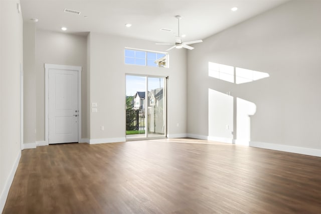 unfurnished living room with ceiling fan, a high ceiling, and dark hardwood / wood-style floors