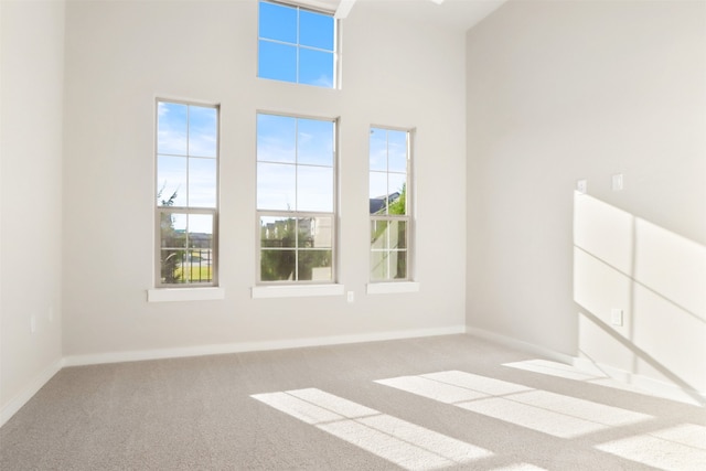 spare room featuring carpet floors, baseboards, a high ceiling, and a healthy amount of sunlight