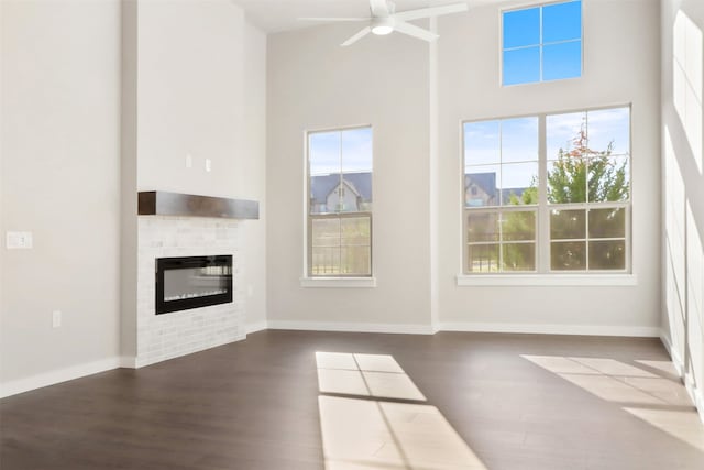 unfurnished living room with dark wood-type flooring, a towering ceiling, and ceiling fan