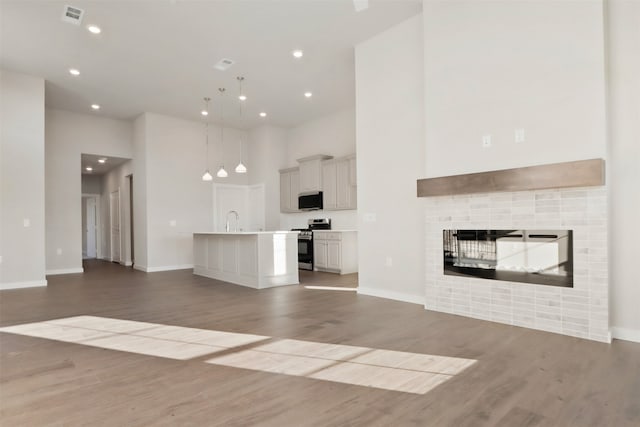 unfurnished living room with a fireplace, baseboards, wood finished floors, a towering ceiling, and visible vents