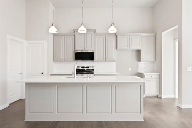 kitchen featuring decorative light fixtures, stainless steel appliances, and an island with sink