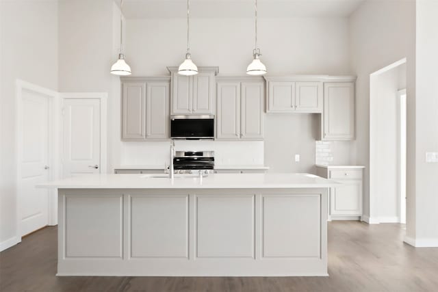kitchen featuring wood finished floors, an island with sink, light countertops, appliances with stainless steel finishes, and hanging light fixtures