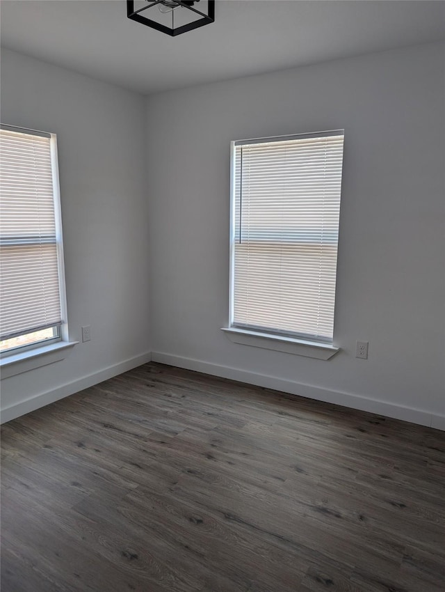 spare room with dark wood-type flooring, an inviting chandelier, and a healthy amount of sunlight