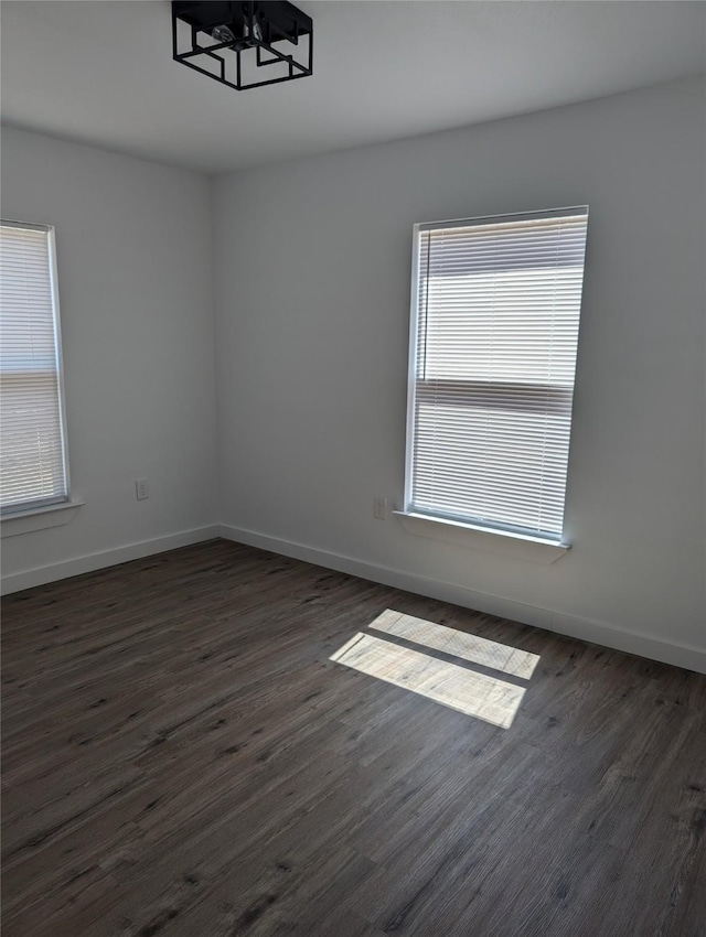 spare room featuring dark wood-type flooring, a wealth of natural light, and a notable chandelier