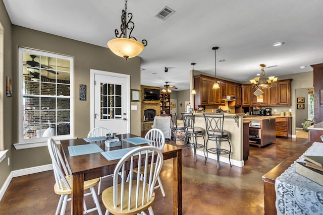 dining space with a large fireplace and ceiling fan with notable chandelier