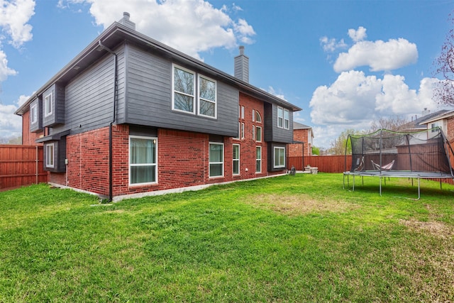 back of property with a trampoline and a yard