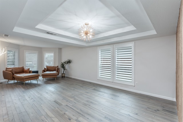 unfurnished room with hardwood / wood-style flooring, a raised ceiling, and a chandelier