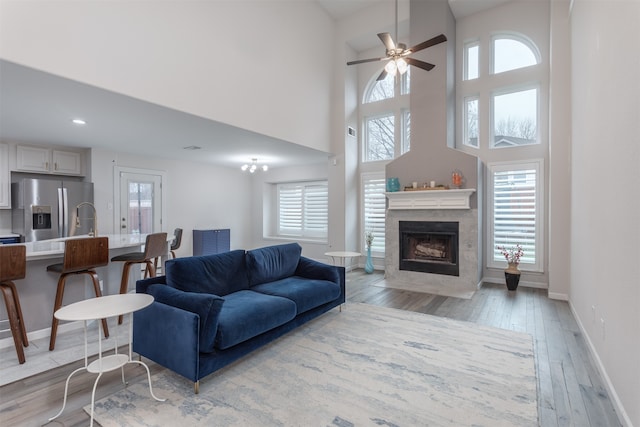 living room featuring a high end fireplace, ceiling fan, light hardwood / wood-style flooring, and a healthy amount of sunlight