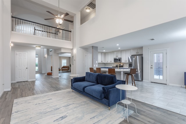 living room featuring a high ceiling, a healthy amount of sunlight, light hardwood / wood-style flooring, and ceiling fan