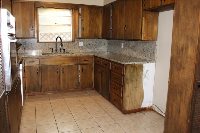 kitchen featuring light tile patterned floors, decorative backsplash, light stone counters, and sink