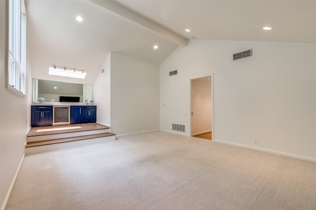 unfurnished living room with beamed ceiling, light colored carpet, a skylight, high vaulted ceiling, and wine cooler