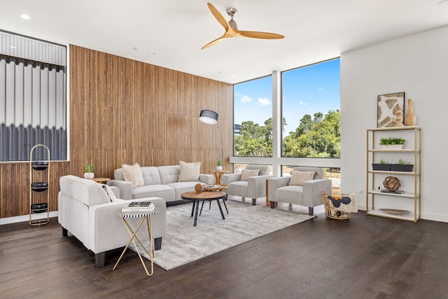 living room with wood walls, a wall of windows, ceiling fan, and dark wood-type flooring