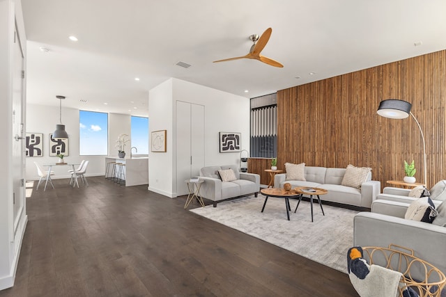 living room with ceiling fan, wooden walls, and wood-type flooring