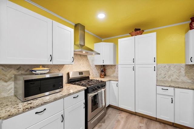 kitchen with white cabinetry, stainless steel appliances, crown molding, and wall chimney range hood