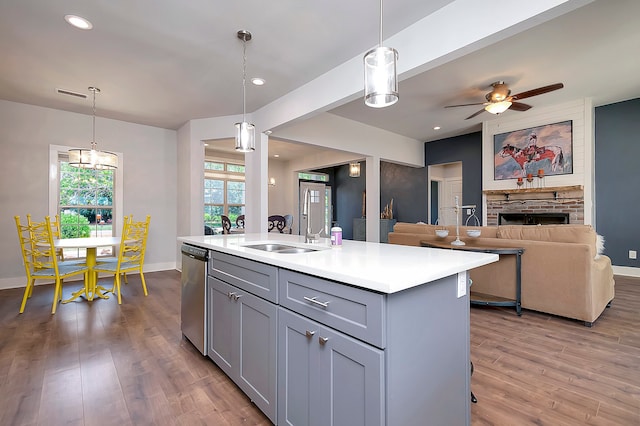 kitchen with an island with sink, stainless steel dishwasher, hanging light fixtures, a fireplace, and wood-type flooring