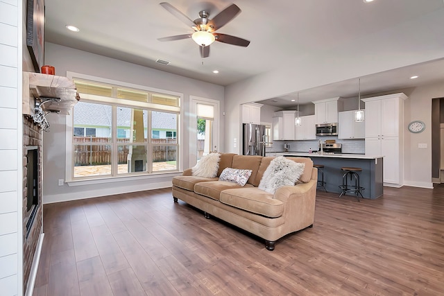 living room featuring a fireplace, ceiling fan, and dark wood-type flooring