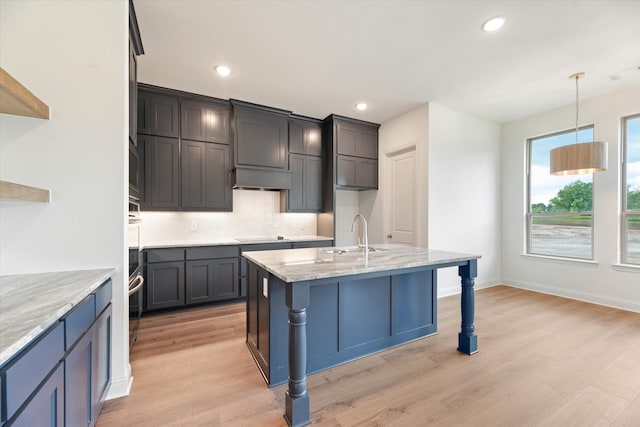 kitchen featuring light stone countertops, light hardwood / wood-style flooring, pendant lighting, sink, and decorative backsplash