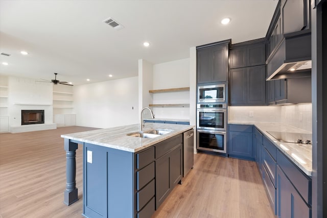 kitchen with a fireplace, light hardwood / wood-style floors, an island with sink, sink, and ceiling fan